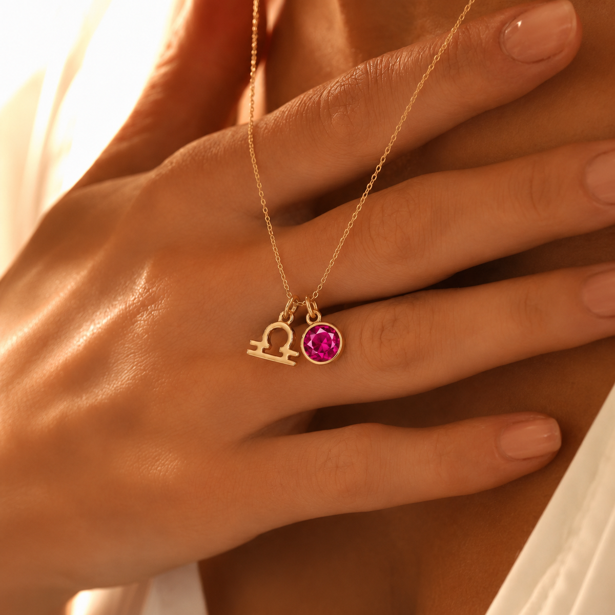 Primer plano de collar dorado personalizado con símbolo del signo Libra y piedra de nacimiento rosa, sujeto sobre el pecho.