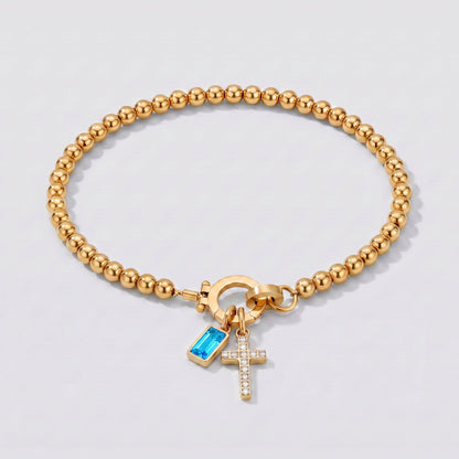 Pulsera dorada de cuentas con cruz y piedra de nacimiento topacio azul de diciembre.