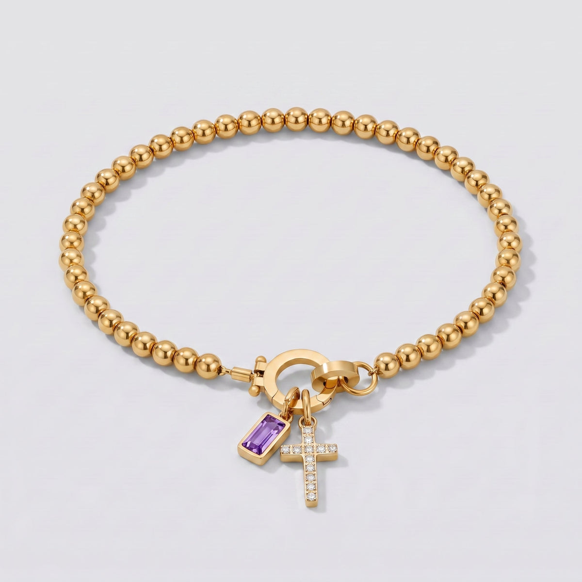 Pulsera dorada de cuentas con cruz y piedra de nacimiento amatista de febrero.