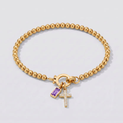 Pulsera dorada de cuentas con cruz y piedra de nacimiento amatista de febrero.