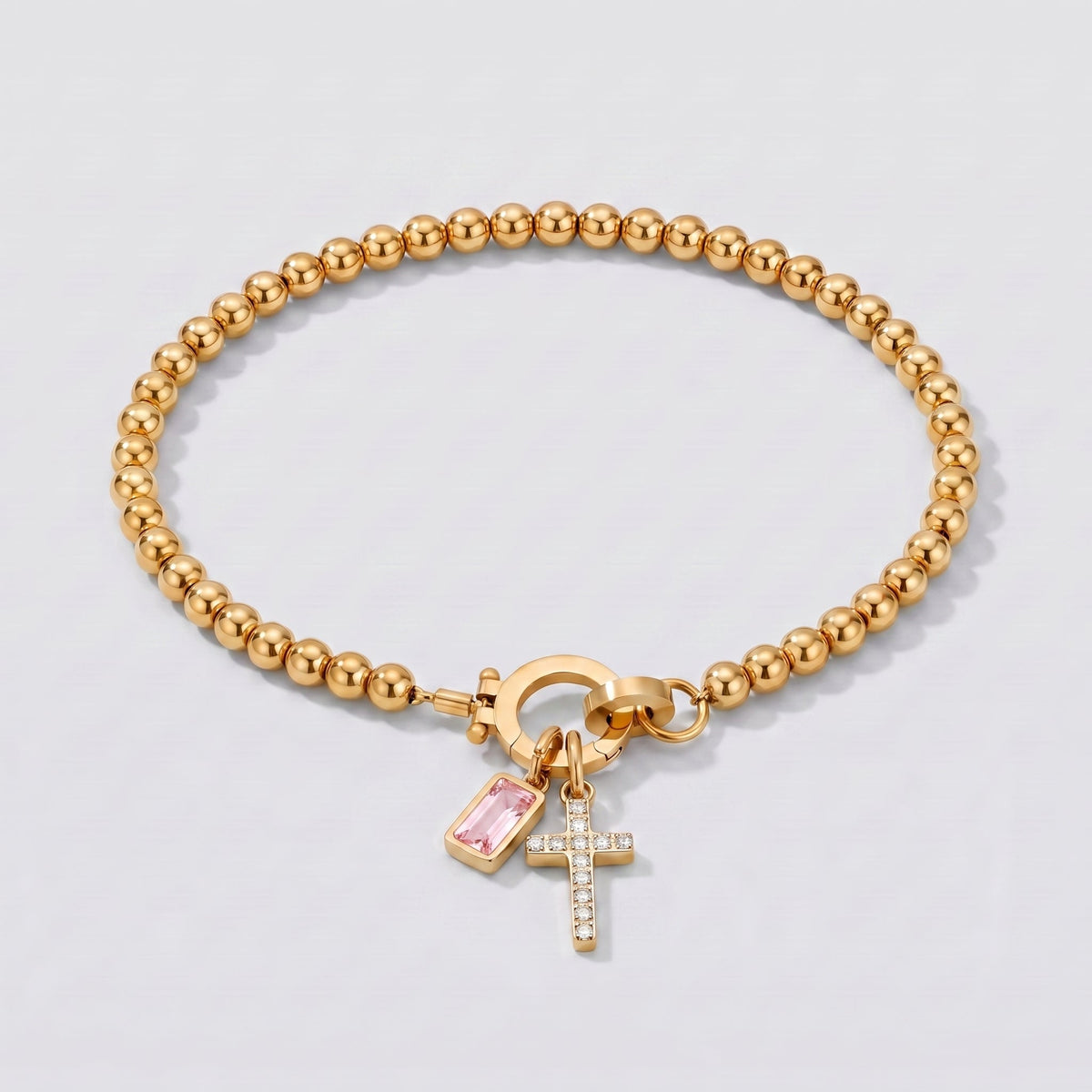 Pulsera dorada de cuentas con cruz y piedra de nacimiento turmalina rosa de octubre.