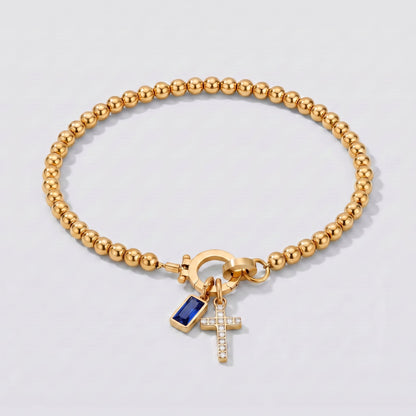 Pulsera dorada de cuentas con cruz y piedra de nacimiento zafiro azul de septiembre.