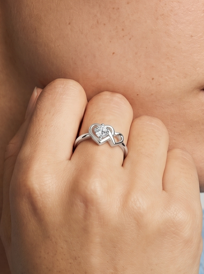 Anillo plateado con un diseño de corazón y un diamante en el dedo de una persona
