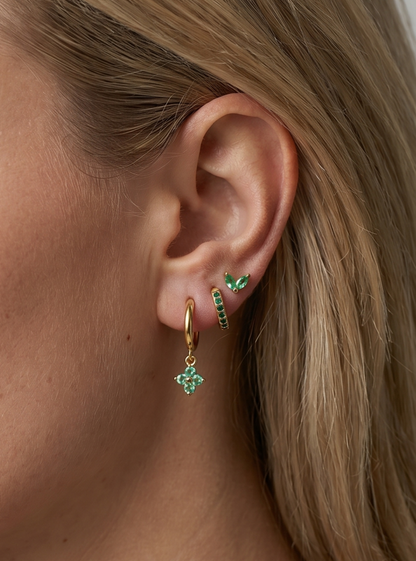 Pendiente de aro dorado y pendiente de presión a juego con detalles en cristal verde, en la oreja de la modelo para un look elegante.
