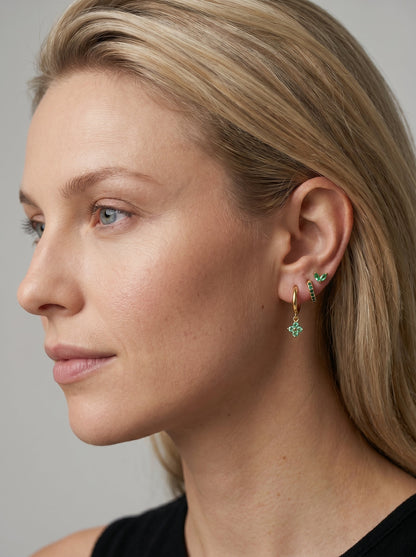 Primer plano de una mujer con pendientes verdes sobre un fondo neutro.
