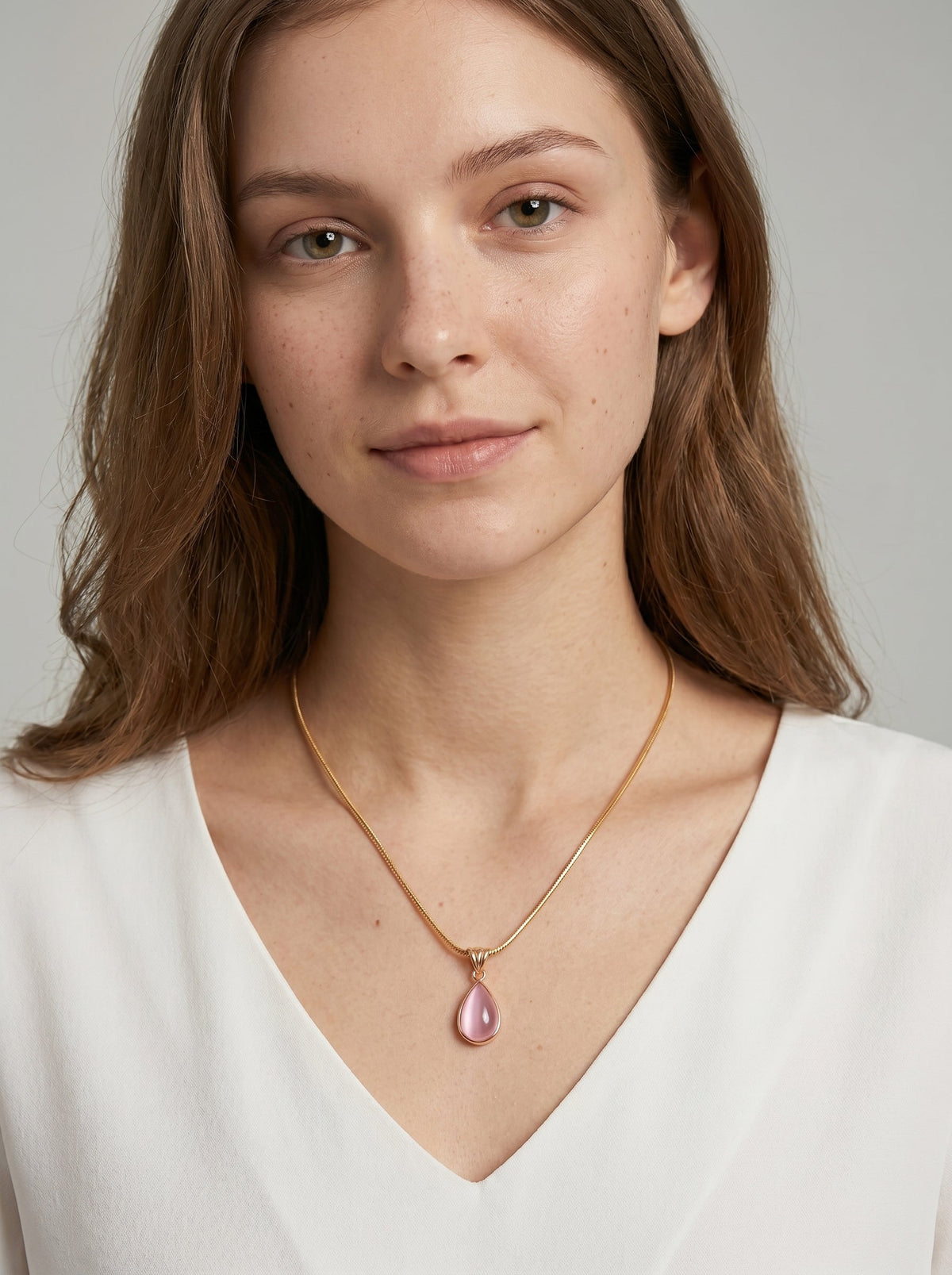 Collar dorado delicado con colgante rosa en forma de gota y acabado elegante, usado por una modelo para un look femenino, sofisticado y delicado.