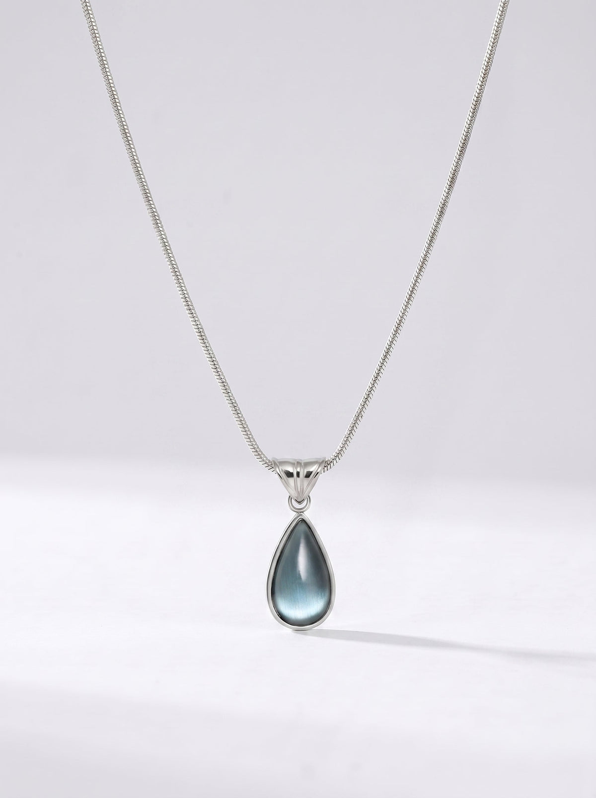 Collar plateado delicado con colgante azul en forma de gota y acabado elegante, fotografiado sobre fondo claro para un look sofisticado, moderno y delicado.