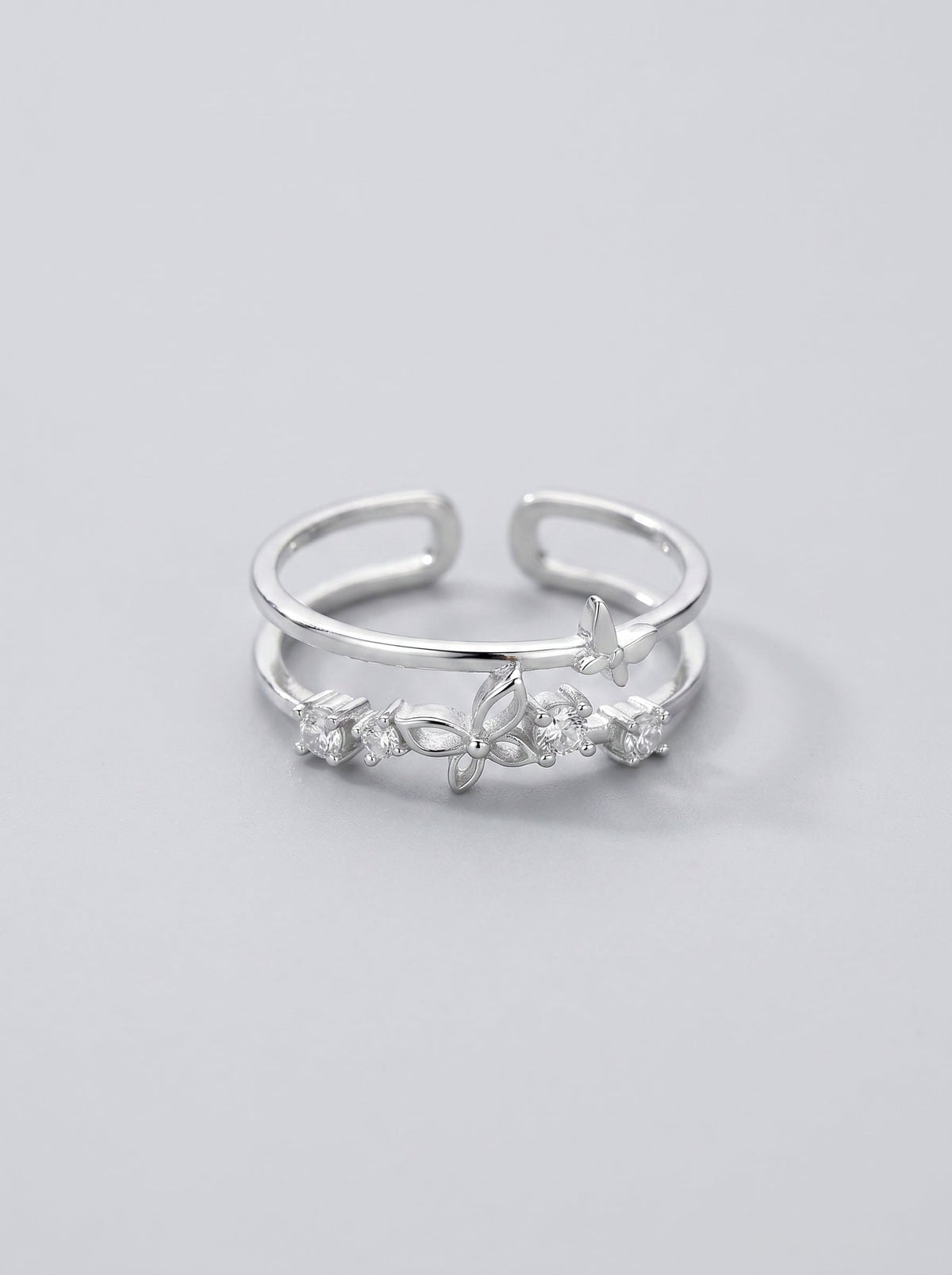 Detalle de un anillo doble en forma de mariposa plateado sobre un fondo gris pizarra.
