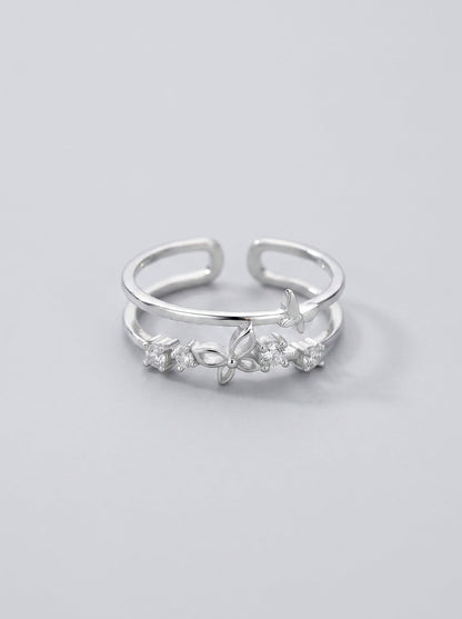Detalle de un anillo doble en forma de mariposa plateado sobre un fondo gris pizarra.
