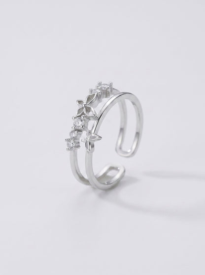 Anillo plateado con piedras preciosas sobre fondo gris claro.
