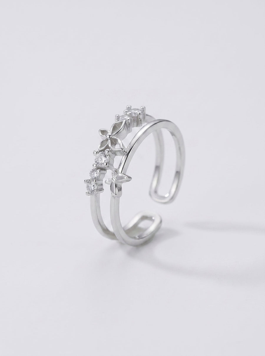 Anillo plateado con piedras preciosas sobre fondo gris claro.
