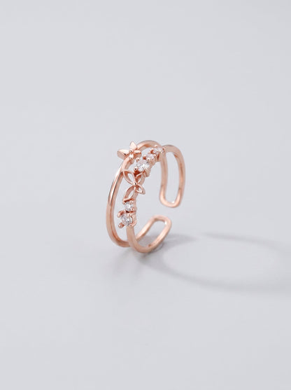 Anillo abierto en oro rosa con diseño floral sobre fondo gris claro.
