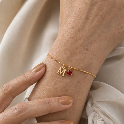 Pulsera letra M dorada en el modelo — piedra Granate