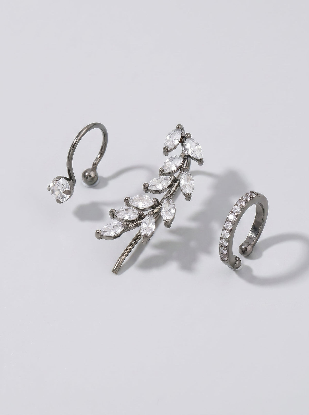 Pendientes de presión con cristales plateados y un delicado detalle en forma de hoja sobre un fondo minimalista gris claro.
