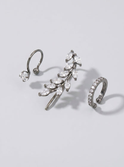 Pendientes de presión con cristales plateados y un delicado detalle en forma de hoja sobre un fondo minimalista gris claro.
