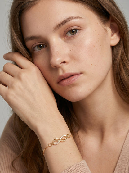 Pulsera dorada delicada con símbolo infinito, cadena fina y acabado brillante, usada por una modelo para un look elegante, femenino y minimalista.