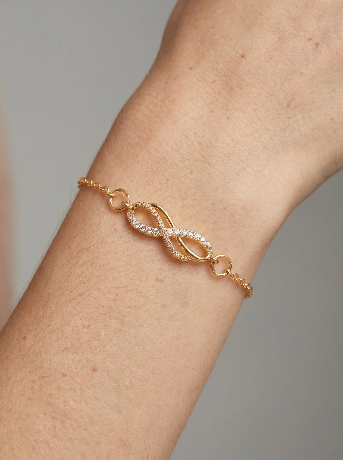Pulsera dorada delicada con símbolo infinito, detalle en cristales y cadena fina, usada en la muñeca para un look elegante, femenino y minimalista.