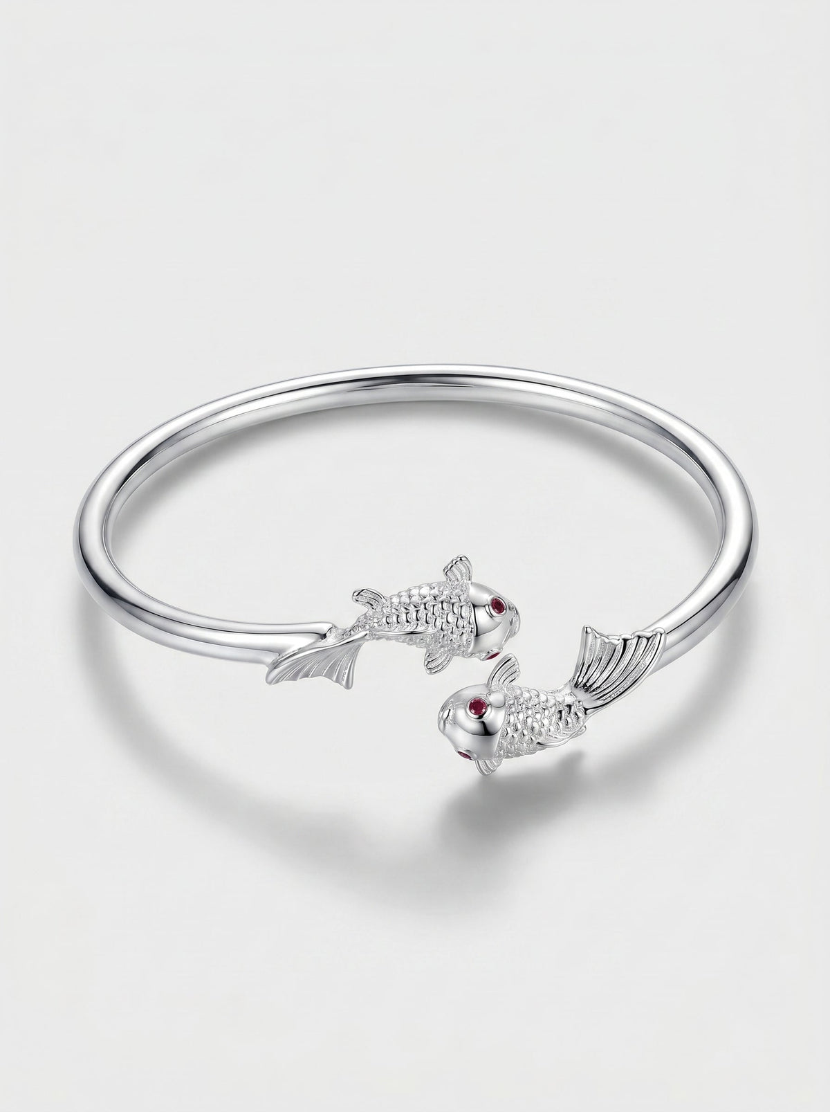 Pulsera plateada rígida con diseño abierto y delicados detalles de peces, fotografiada sobre fondo claro para un look elegante y minimalista.