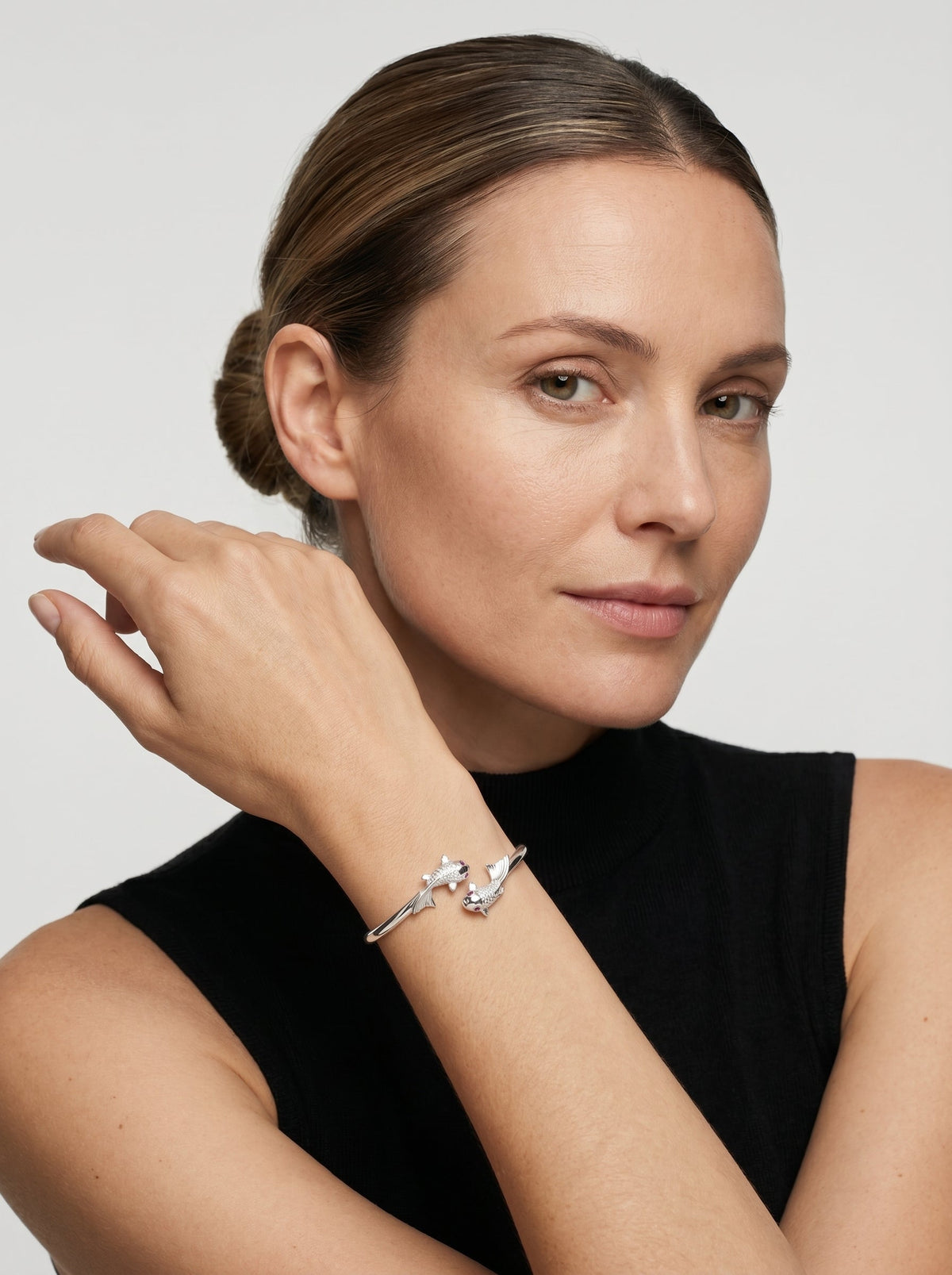 Pulsera plateada rígida con diseño abierto y delicados detalles de peces, usada por una modelo para un look elegante y minimalista.