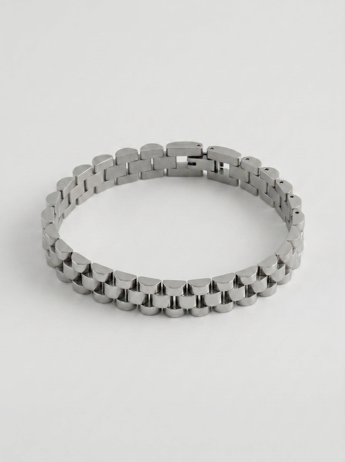 Pulsera plateada con diseño de eslabones anchos y acabado pulido, fotografiada sobre fondo gris claro para un look elegante y sofisticado.