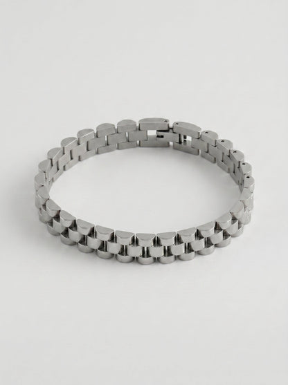 Pulsera plateada con diseño de eslabones anchos y acabado pulido, fotografiada sobre fondo gris claro para un look elegante y sofisticado.