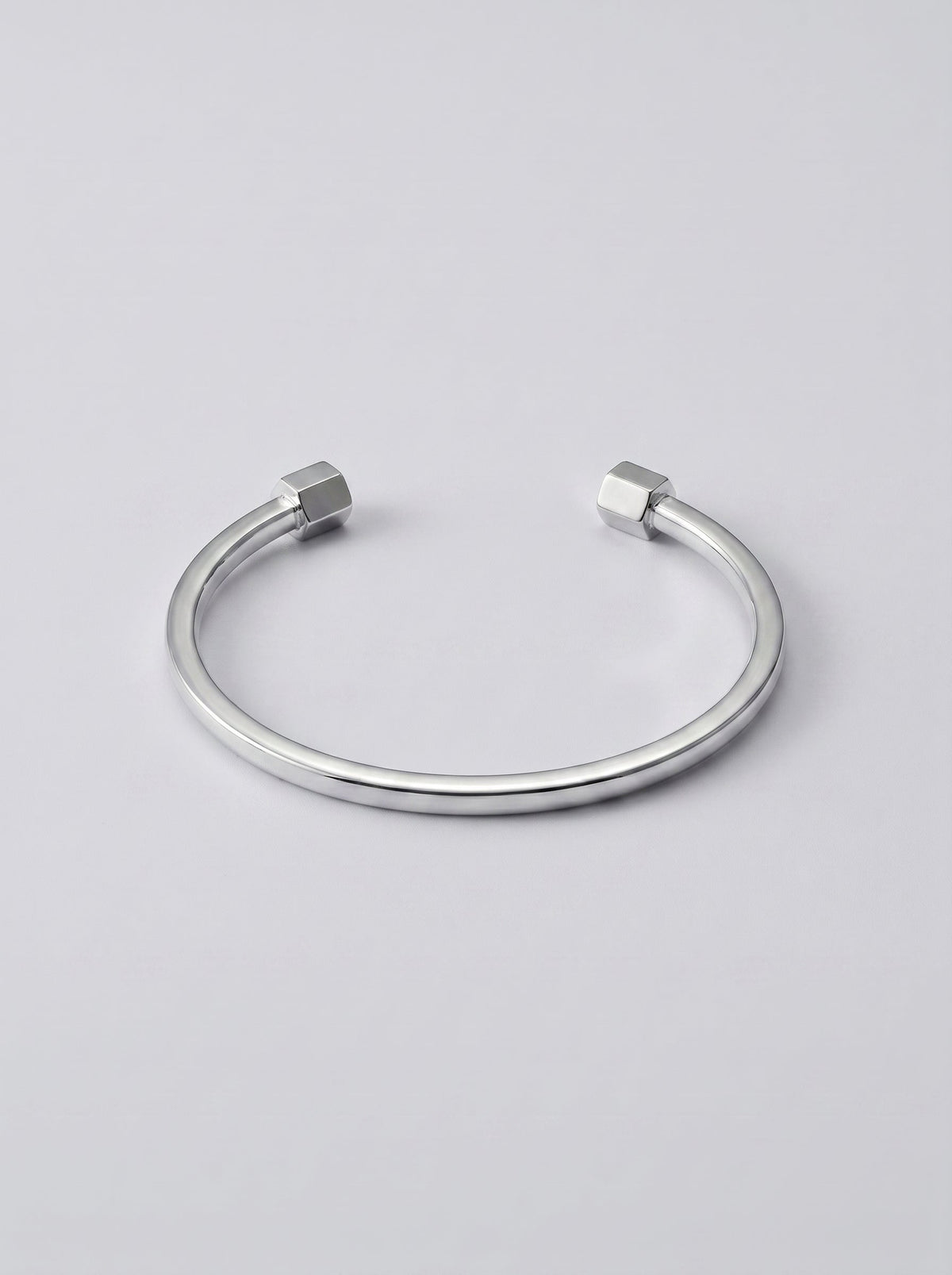 Pulsera plateada abierta con extremos en forma de hexágono sobre fondo gris claro.