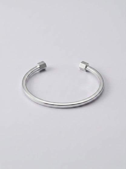 Pulsera plateada abierta con extremos en forma de hexágono sobre fondo gris claro.