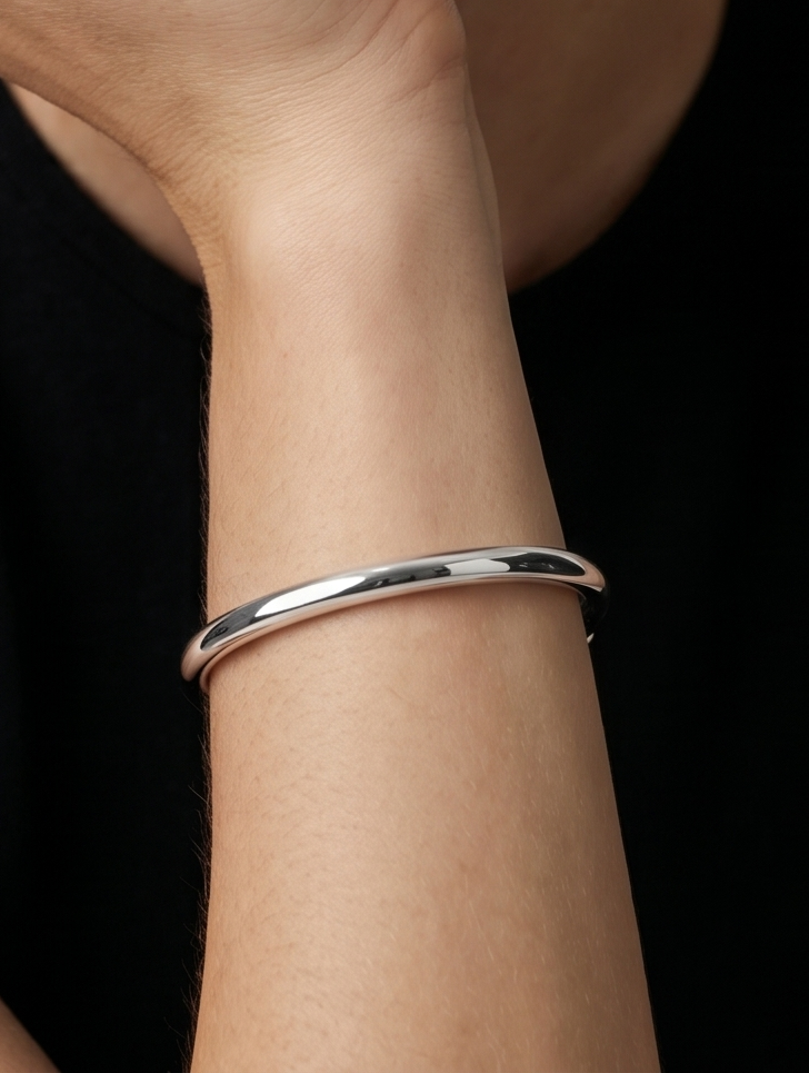 Pulsera plateada rígida con diseño abierto, acabado pulido y extremos hexagonales, usada en la muñeca para un look minimalista y moderno.