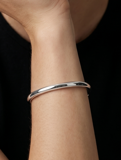 Pulsera plateada rígida con diseño abierto, acabado pulido y extremos hexagonales, usada en la muñeca para un look minimalista y moderno.