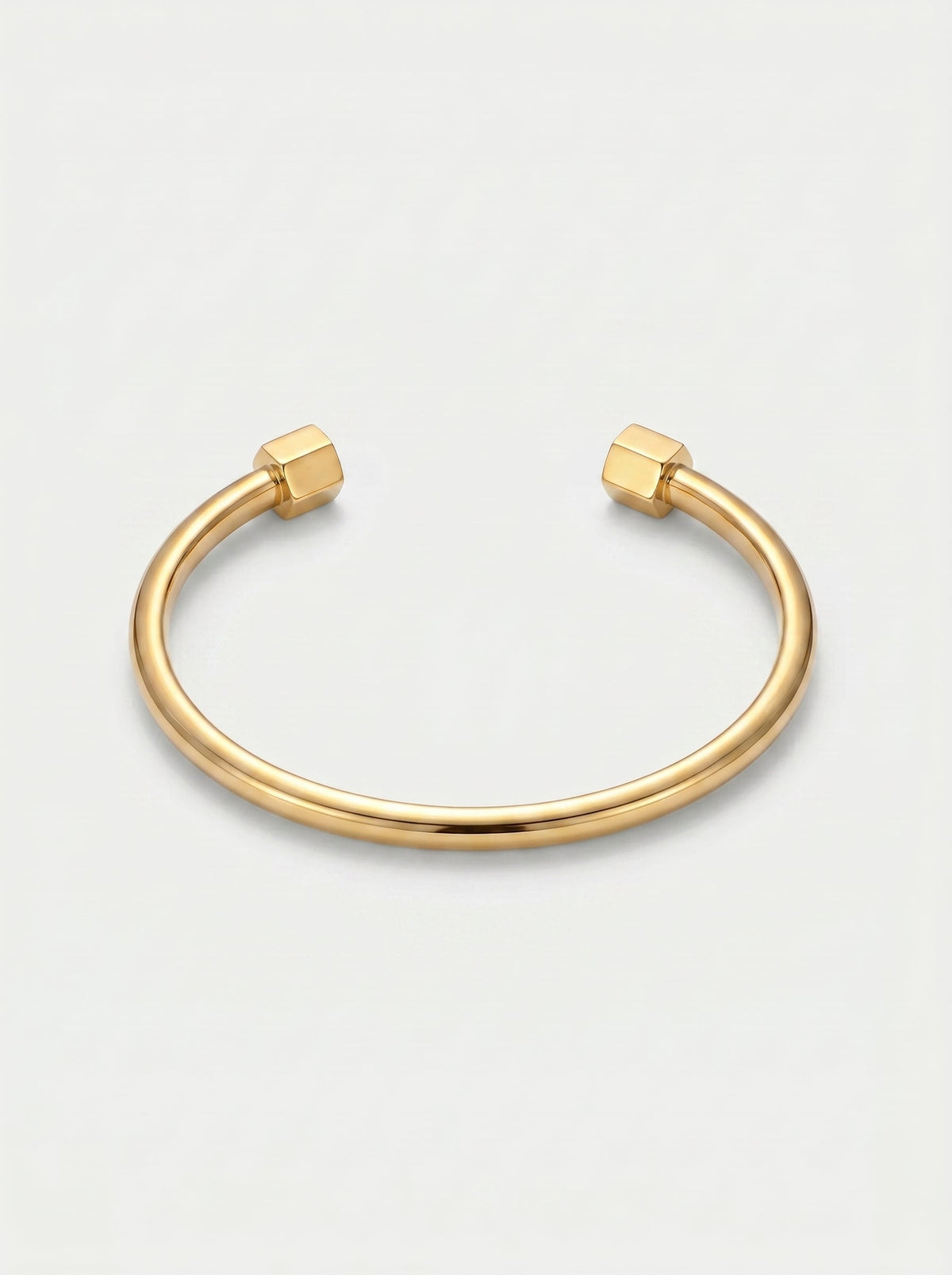 Pulsera dorada rígida con diseño abierto, acabado pulido y extremos hexagonales, fotografiada sobre fondo claro para un look minimalista y moderno.