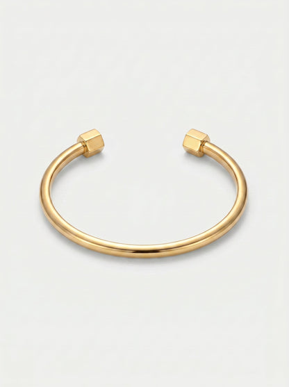Pulsera dorada rígida con diseño abierto, acabado pulido y extremos hexagonales, fotografiada sobre fondo claro para un look minimalista y moderno.
