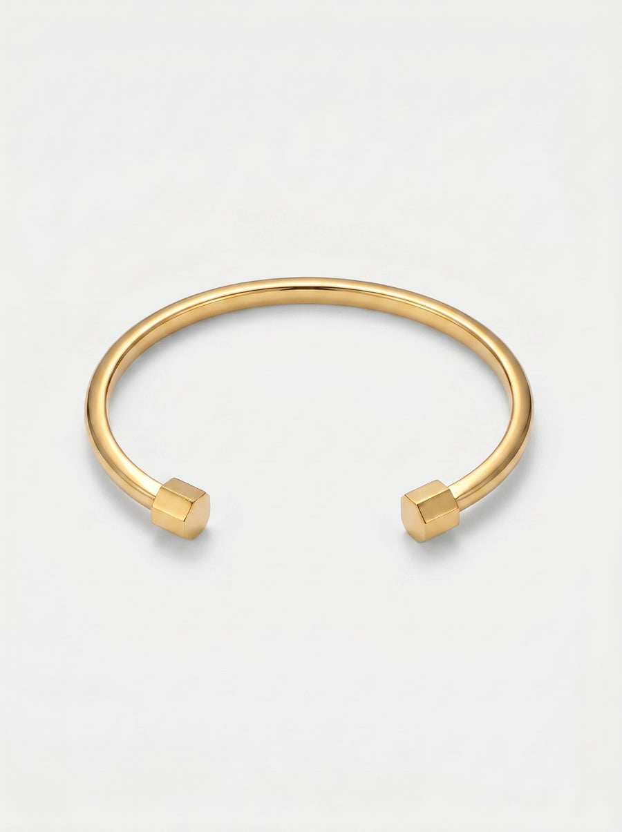 Pulsera dorada rígida con diseño abierto, acabado pulido y extremos hexagonales, fotografiada sobre fondo claro para un look minimalista y moderno.