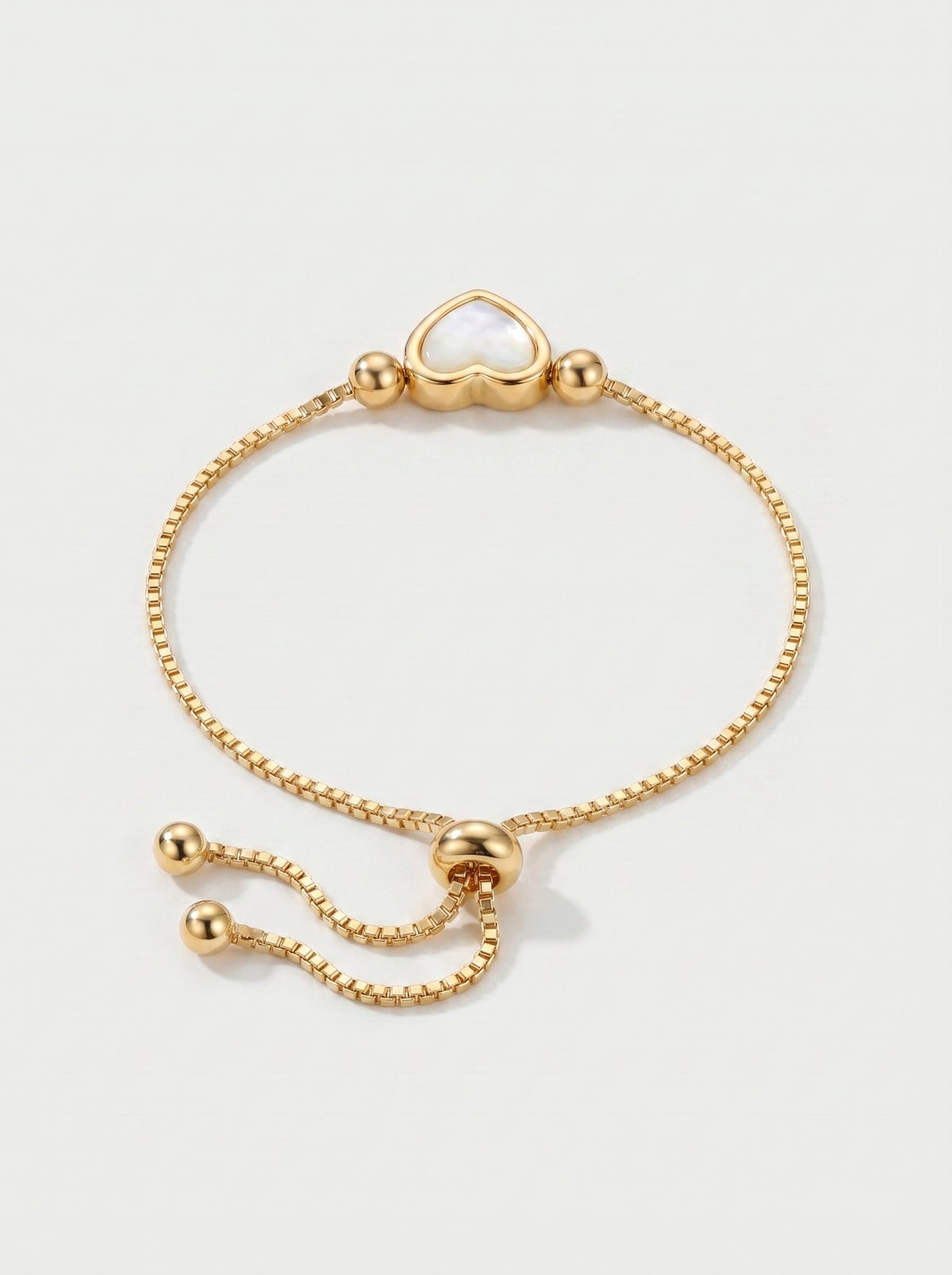 Pulsera dorada delicada con colgante en forma de corazón blanco, cadena ajustable y acabado brillante, fotografiada sobre fondo claro para un look elegante, femenino y romántico.