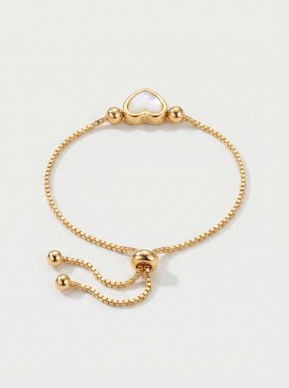 Pulsera dorada delicada con colgante en forma de corazón blanco, cadena ajustable y acabado brillante, fotografiada sobre fondo claro para un look elegante, femenino y romántico.