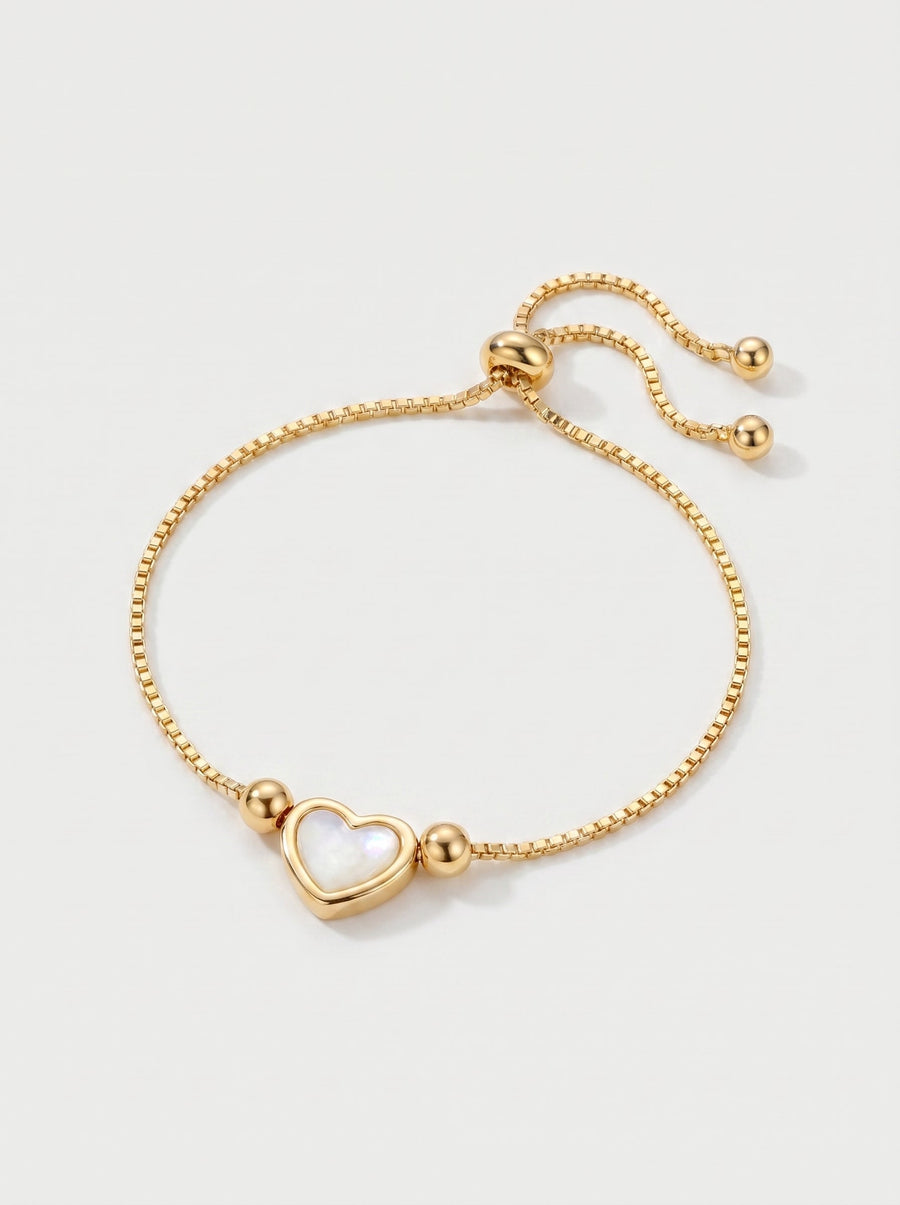 Pulsera dorada delicada con colgante en forma de corazón blanco, cadena ajustable y acabado brillante, fotografiada sobre fondo claro para un look elegante, femenino y romántico.