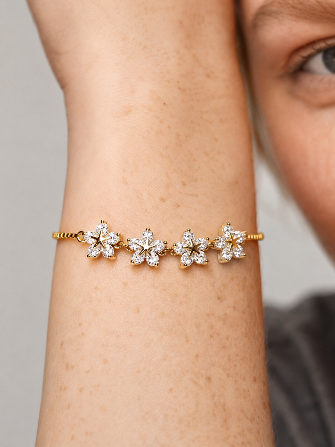 Pulsera dorada elegante con flores de cristales brillantes y cadena fina, usada en la muñeca para un look femenino, delicado y luminoso.