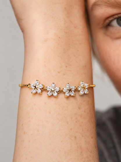 Pulsera dorada elegante con flores de cristales brillantes y cadena fina, usada en la muñeca para un look femenino, delicado y luminoso.