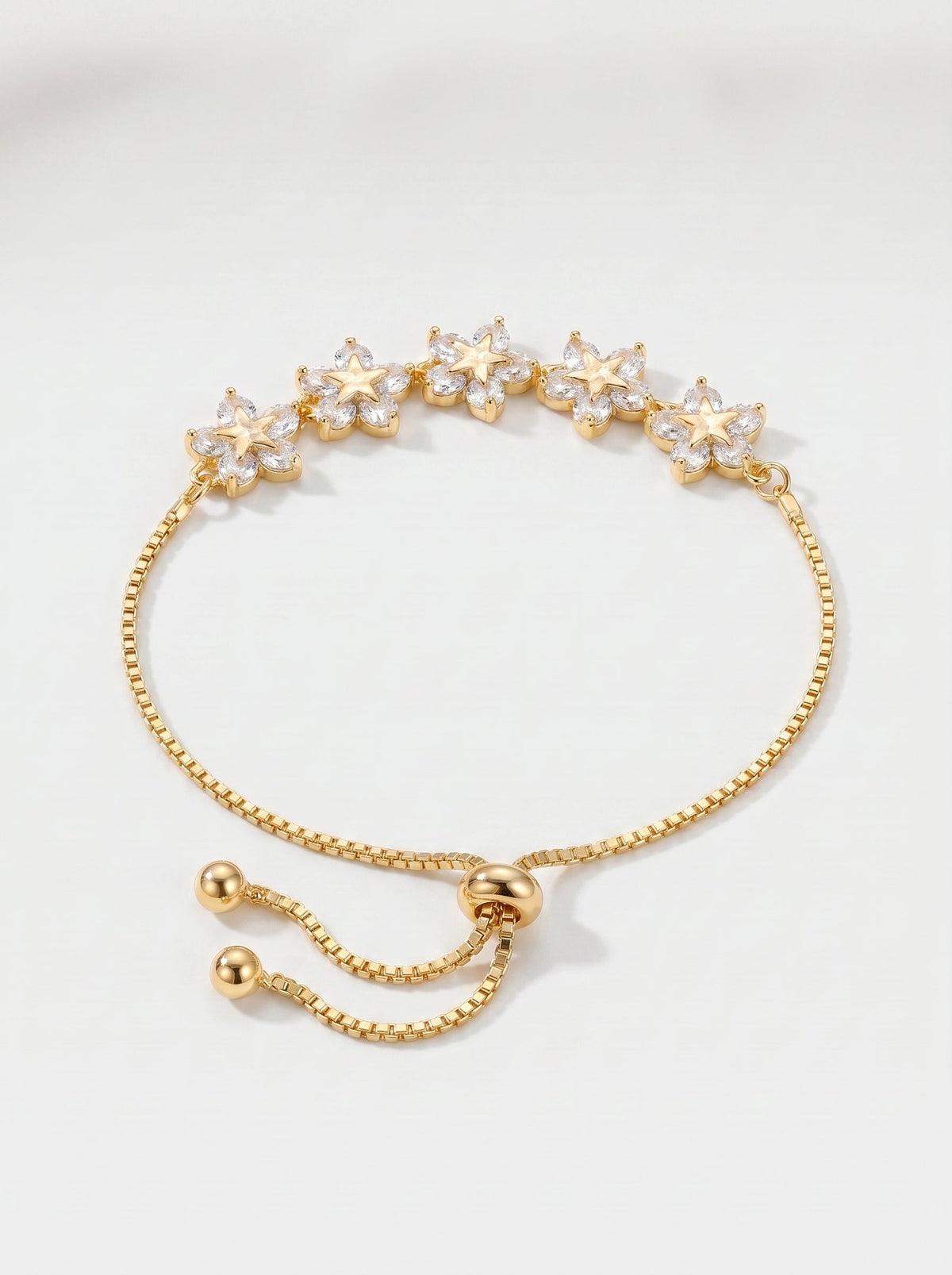 Pulsera dorada delicada con flores de cristales, cadena ajustable y acabado brillante, fotografiada sobre fondo claro para un look femenino, elegante y luminoso.