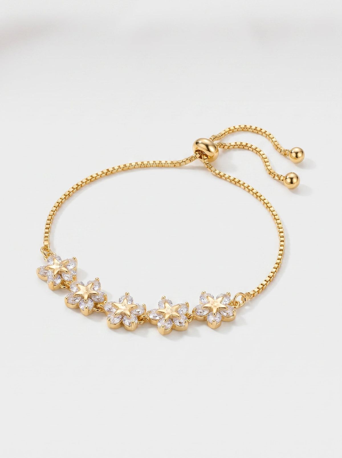 Pulsera dorada delicada con flores de cristales, cadena ajustable y acabado brillante, fotografiada sobre fondo claro para un look femenino, elegante y luminoso.
