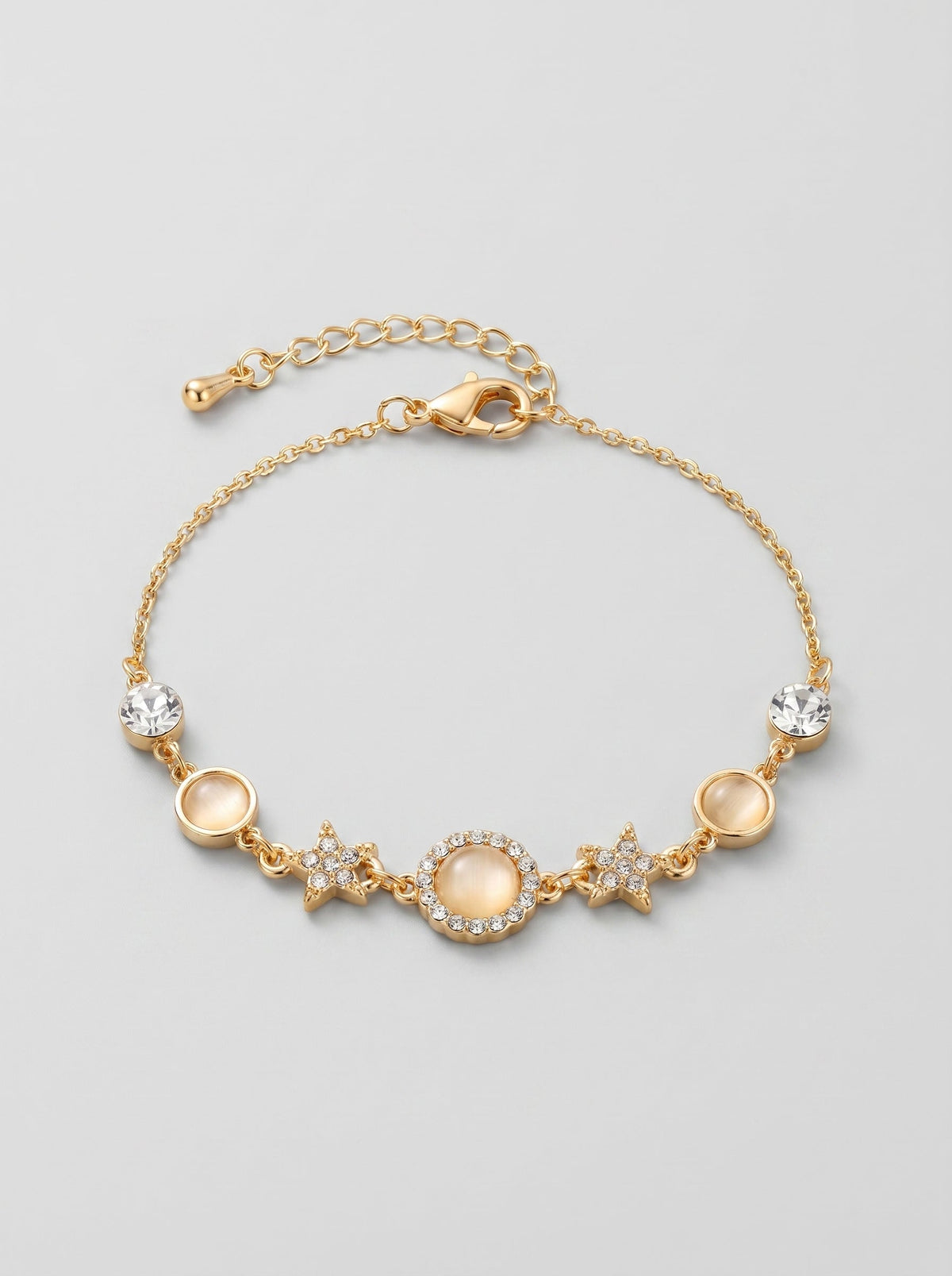 Pulsera dorada delicada con cristales brillantes, detalles en estrella y colgante circular central, fotografiada sobre fondo gris claro para un look elegante, femenino y sofisticado.