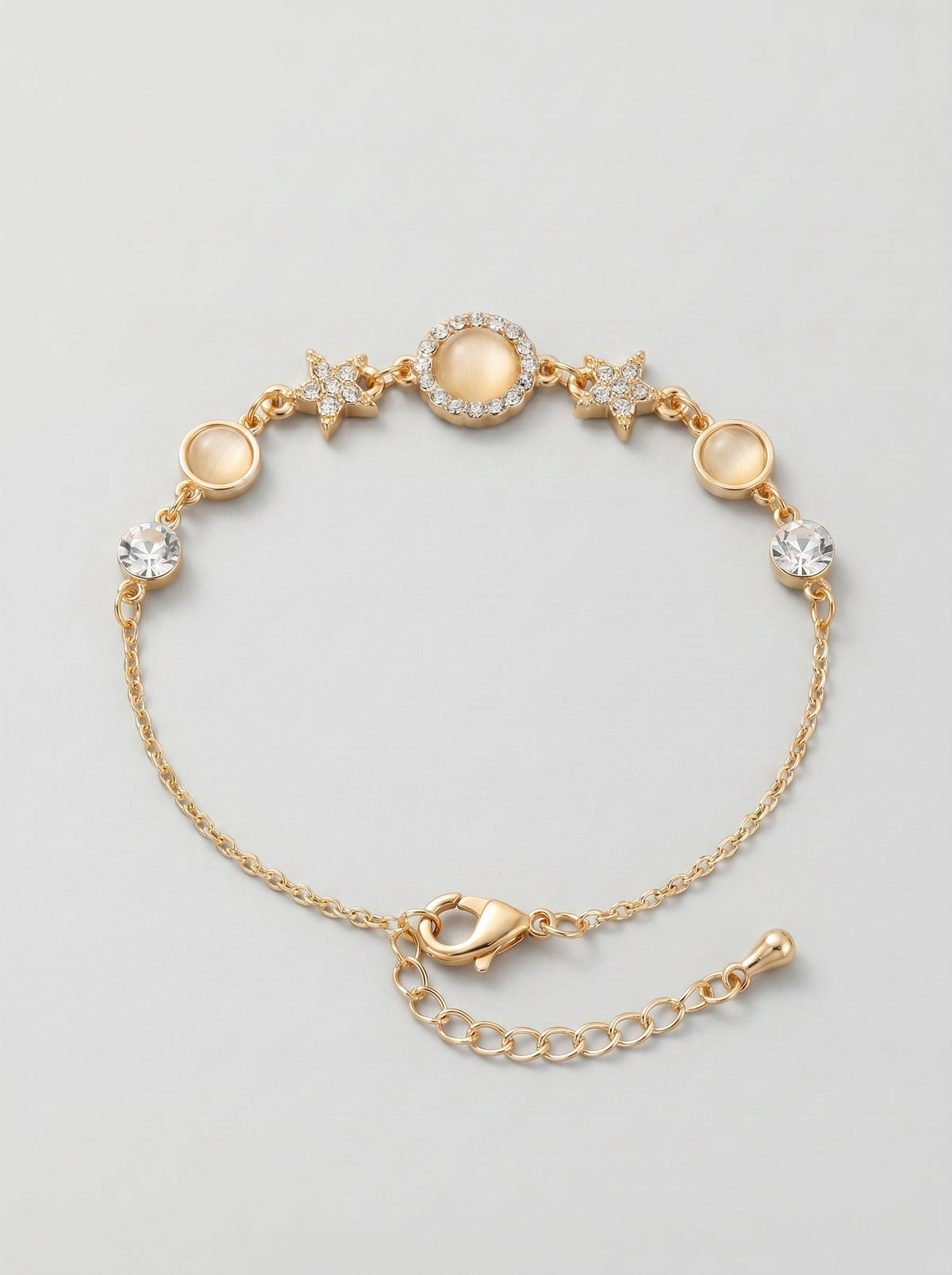 Pulsera dorada delicada con cristales brillantes, detalles en estrella y colgante circular central, fotografiada sobre fondo gris claro para un look elegante, femenino y sofisticado.