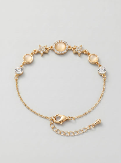 Pulsera dorada delicada con cristales brillantes, detalles en estrella y colgante circular central, fotografiada sobre fondo gris claro para un look elegante, femenino y sofisticado.