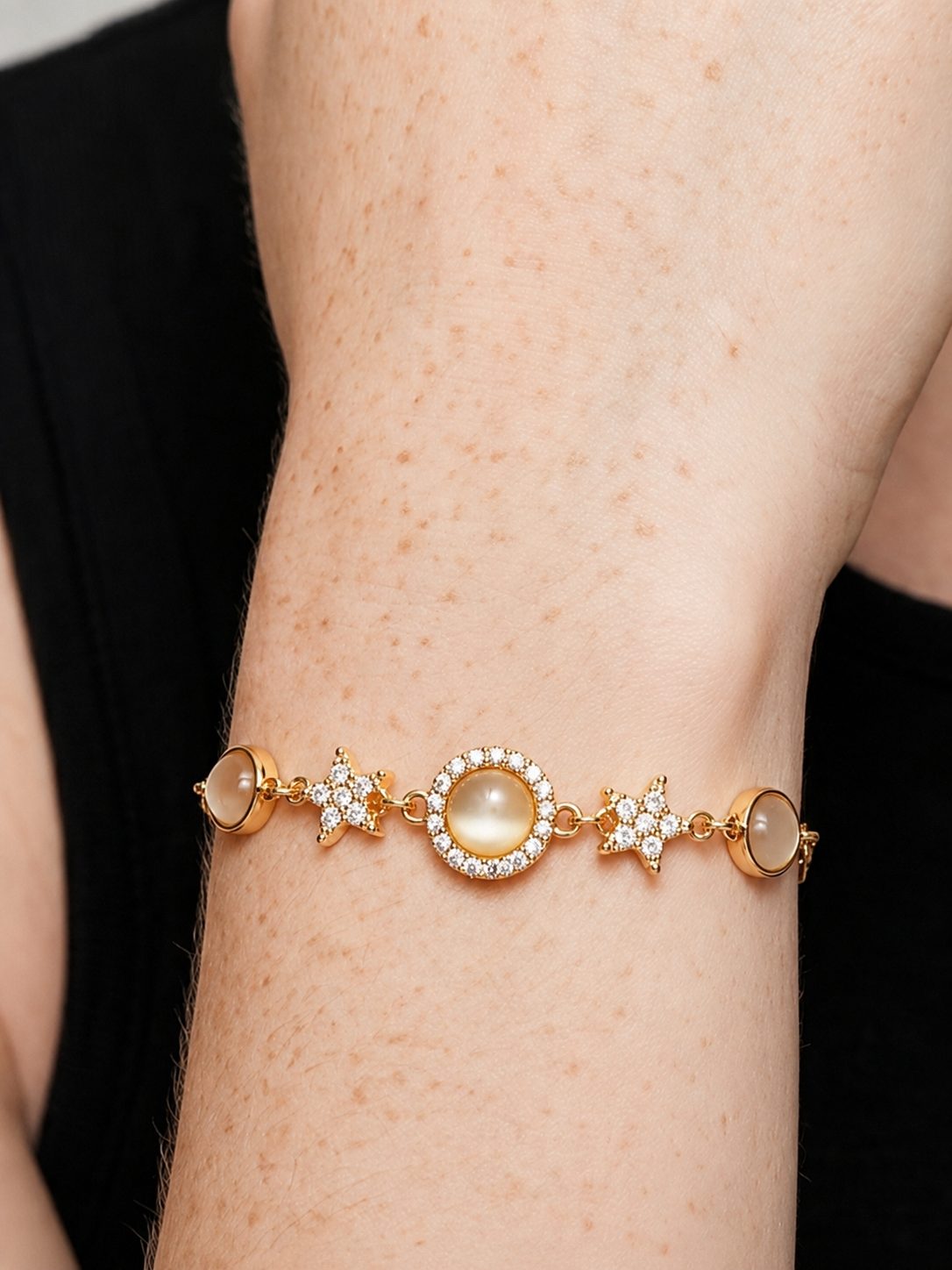 Pulsera dorada elegante con cristales brillantes, detalles en estrella y colgante circular central, en la muñeca para un look femenino, sofisticado y luminoso.