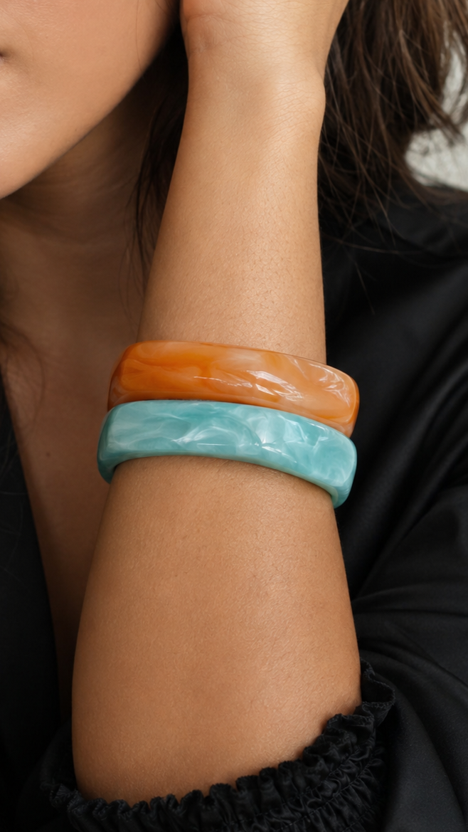 Pulseras de resina en azul turquesa y naranja usadas en la muñeca, con acabado brillante y estilo elegante.